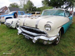 Cream and turquoise vintage Pontiac on a grassy field at a car show, with a shiny chrome grille and bumper in the foreground.