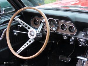 Vintage car interior with a wooden steering wheel and chrome dashboard gauges.