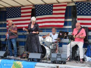 Live band performing on stage with three musicians and large American flag banners as backdrop